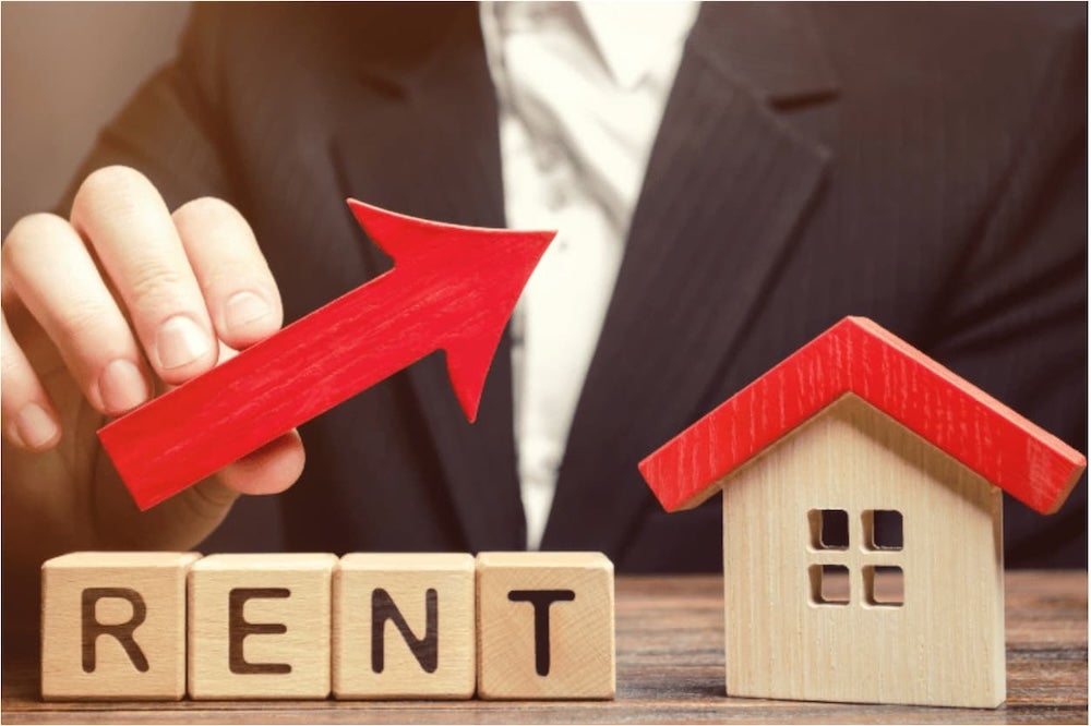 An image of a toy wooden house and the word rent in wooden blocks with someone holding an arrow indicating rent increases