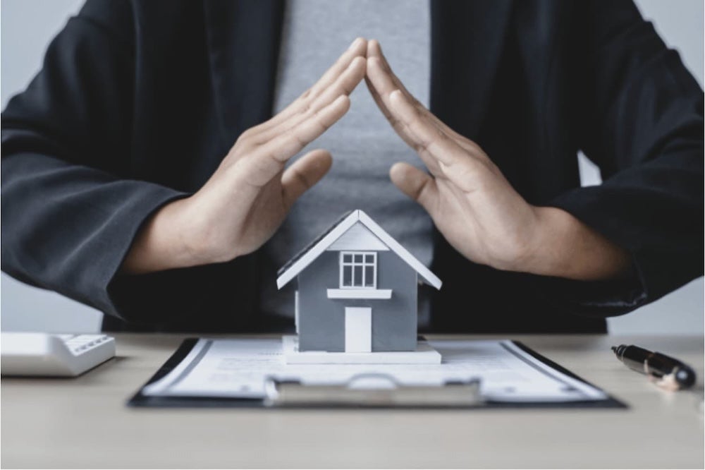 An image of hands over a model house