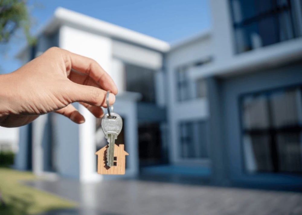 Someone holding a set of keys infront of a house