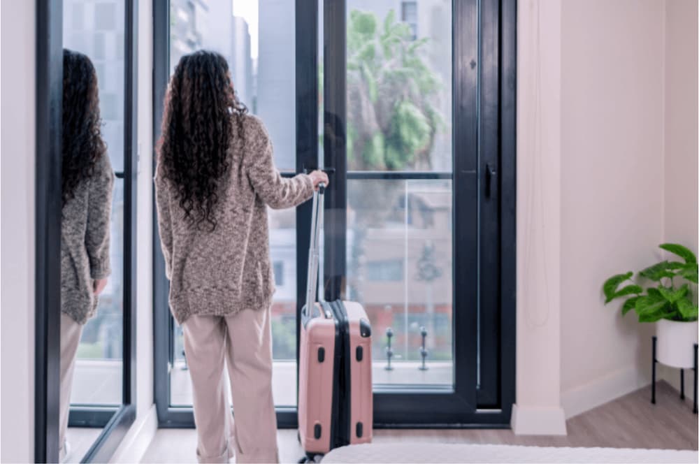 A woman stood by a door with a suitcase