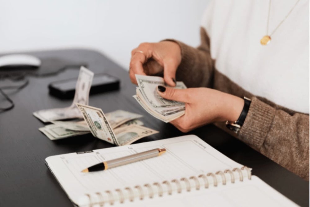 An image of someone counting cash at a desk with pen and paper