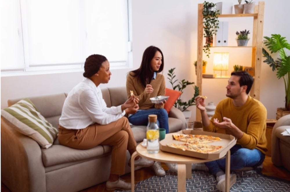 Three roommates around a table in the living room sharing pizza