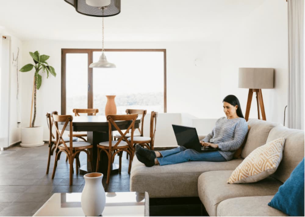 An image of a woman sat on a couch on a laptop in the living room