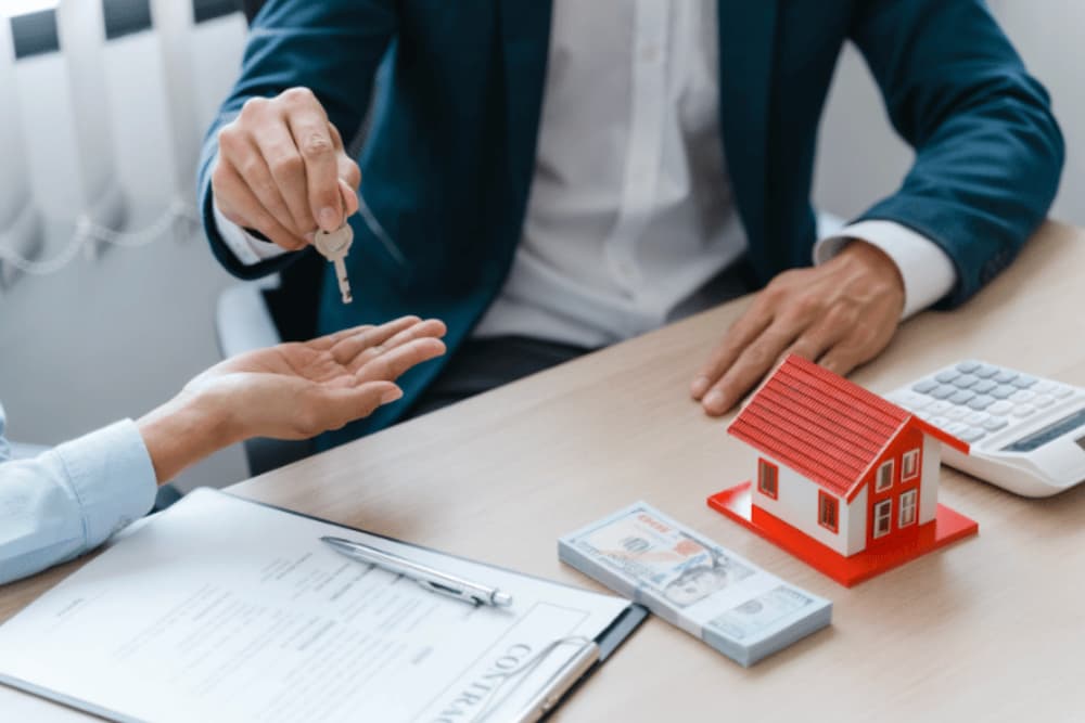 Two people sat at a desk and someone handing keys to the other person
