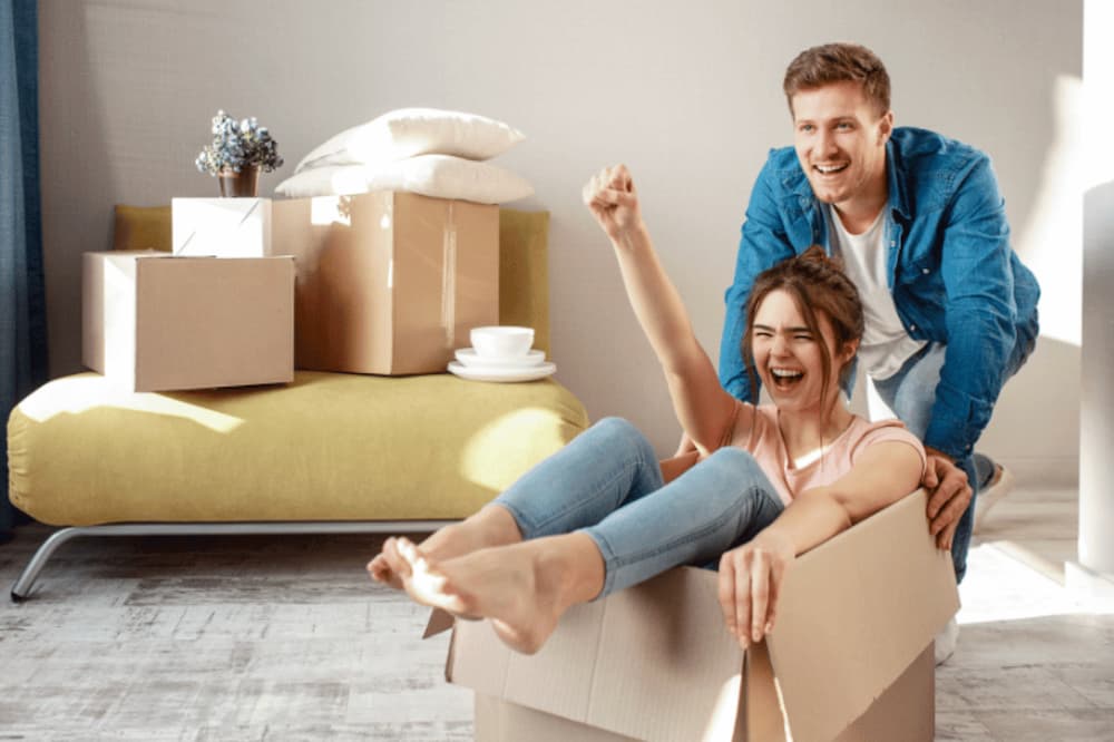 A man pushing a box across the floow with a woman in a playful manor