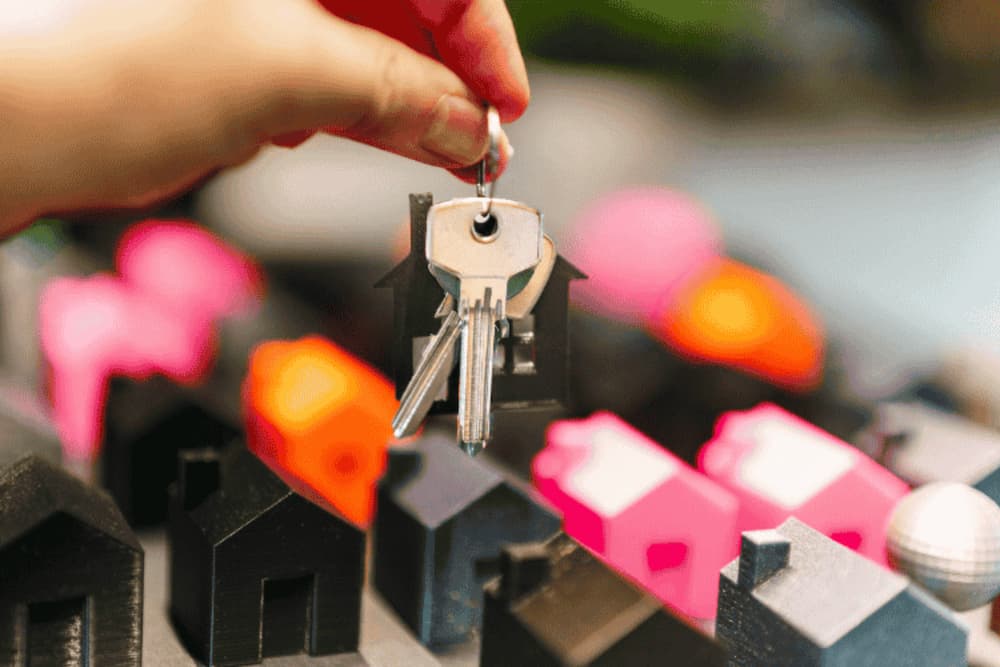 An image of someone holding up a set of keys above a model housing complex