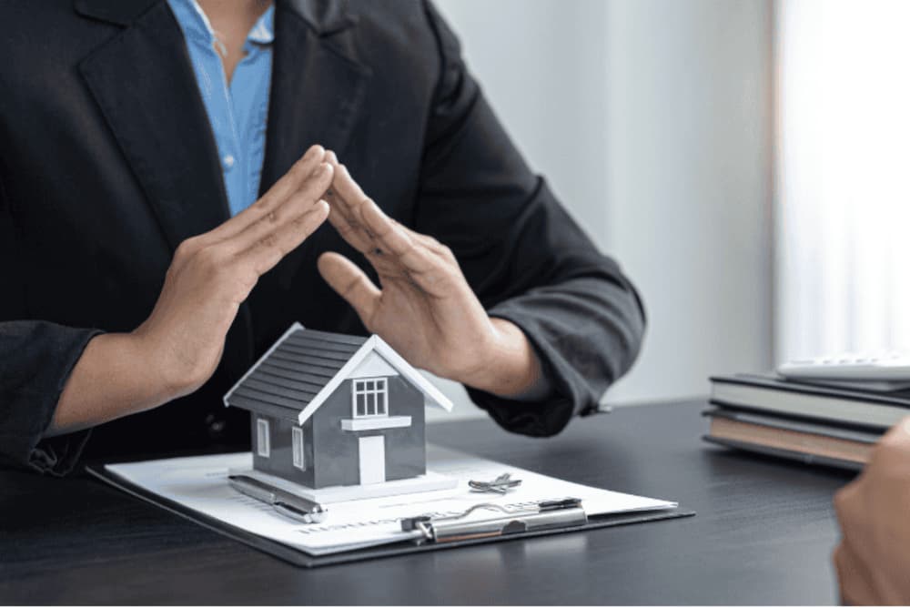 An image of someone making a roof with their hands over a small model house on a desk