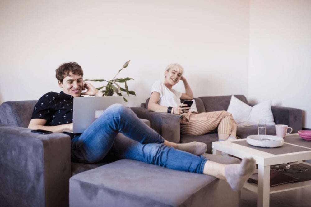 Two roommates relaxing on the couch on a laptop and phone