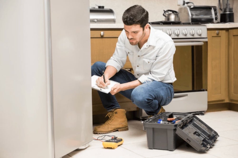 A man with a tool box looking at kitchen appliances