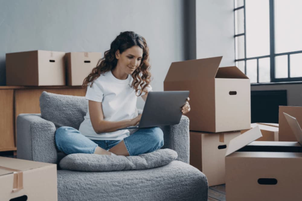 An image of someone sat in a chair surrounded by removal boxes using a laptop