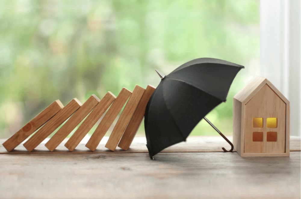 An image of a small model umbrella shielding a wooden model house from falling wooden dominoes