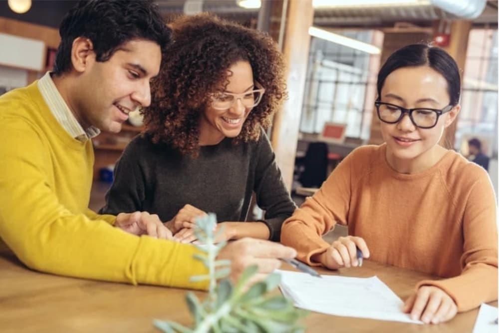 An image of three people sat around a table with a document on
