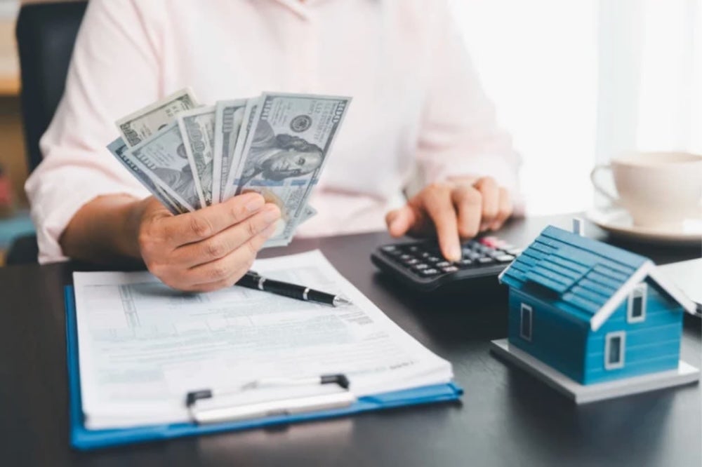 An image of someone at a desk with cash in hand a calculator and a clipboard with forms attached