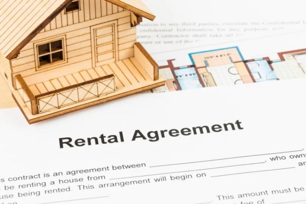 An image of a wooden model house on top of a renatal agreement document